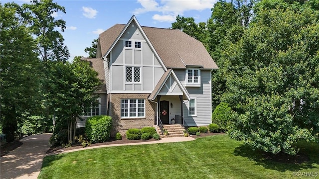 tudor house featuring a shingled roof, a front lawn, and brick siding