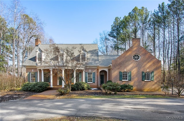 cape cod-style house featuring a chimney and brick siding