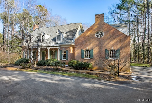 new england style home featuring a chimney and brick siding