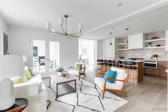 living area featuring french doors, light wood-type flooring, and an inviting chandelier