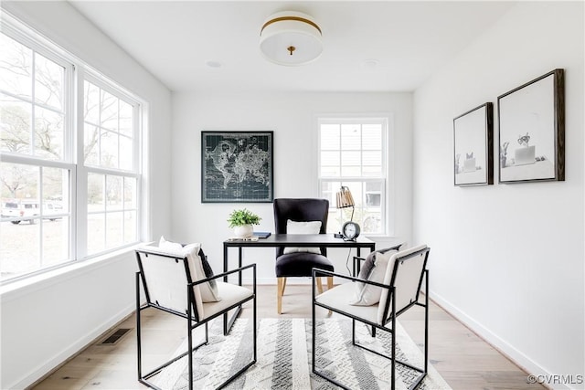 office space featuring baseboards, a healthy amount of sunlight, visible vents, and light wood-style floors