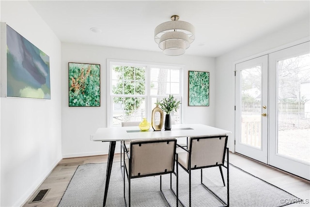 dining room with light wood finished floors, baseboards, visible vents, and french doors