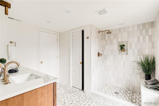 bathroom with double vanity, tiled shower, a sink, and visible vents