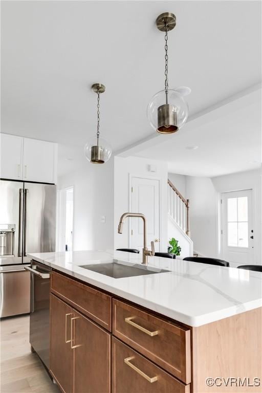 kitchen featuring a center island with sink, light wood-style flooring, appliances with stainless steel finishes, decorative light fixtures, and a sink