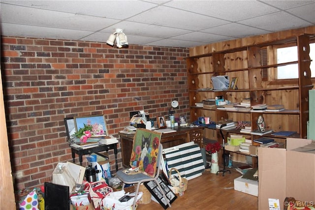 interior space with a paneled ceiling, brick wall, and wood finished floors