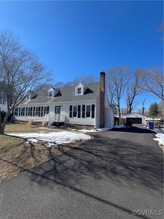 new england style home featuring an outbuilding, driveway, and a chimney