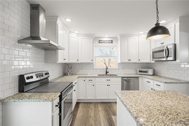 kitchen with a sink, white cabinets, appliances with stainless steel finishes, wall chimney exhaust hood, and decorative light fixtures