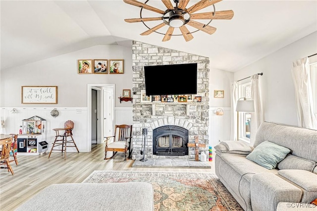 living room with ceiling fan, lofted ceiling, a stone fireplace, and light wood-type flooring