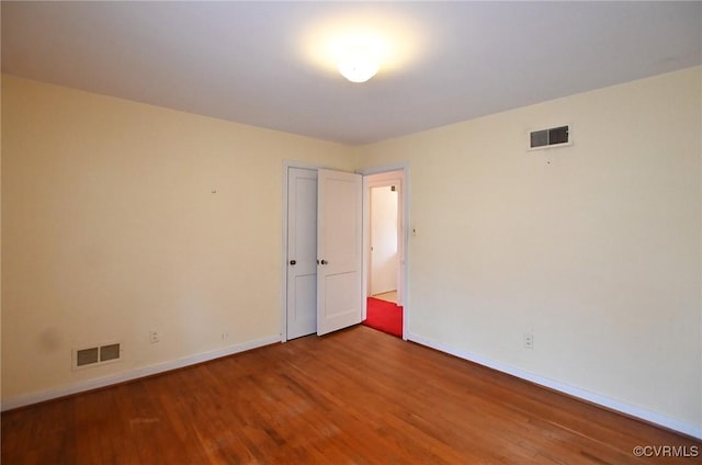 spare room with wood finished floors, visible vents, and baseboards