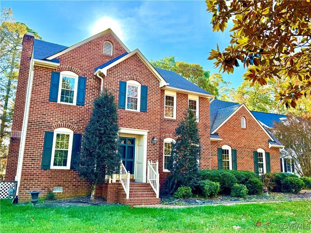 colonial home with roof with shingles, brick siding, a chimney, and a front yard