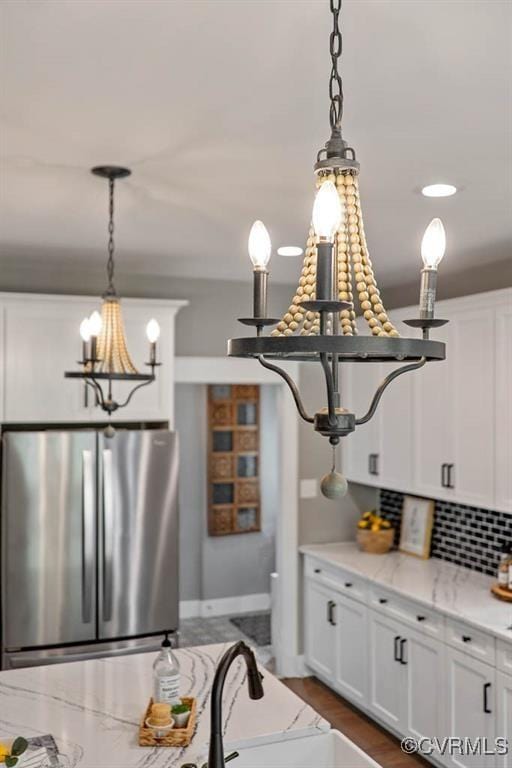 kitchen featuring tasteful backsplash, white cabinets, decorative light fixtures, freestanding refrigerator, and a notable chandelier