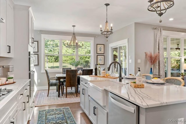 kitchen with a notable chandelier, stainless steel appliances, a sink, white cabinetry, and a center island with sink