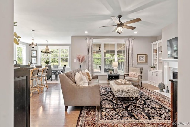 living area featuring baseboards, a premium fireplace, wood finished floors, ceiling fan with notable chandelier, and recessed lighting