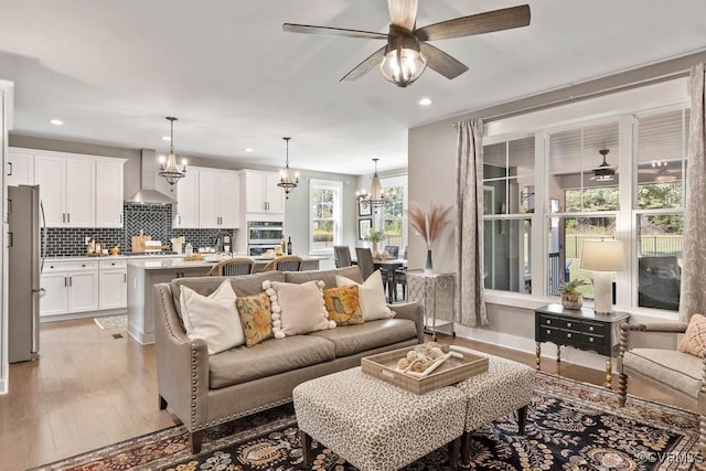 living area featuring light wood-type flooring, baseboards, recessed lighting, and ceiling fan with notable chandelier