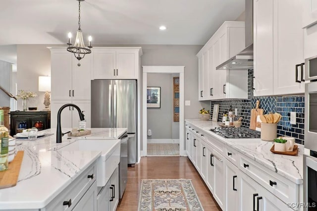 kitchen with light wood finished floors, tasteful backsplash, appliances with stainless steel finishes, white cabinetry, and wall chimney exhaust hood