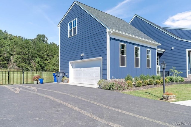 view of side of property featuring a garage, aphalt driveway, roof with shingles, fence, and board and batten siding