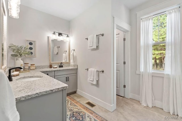 full bath featuring two vanities, a sink, visible vents, and baseboards