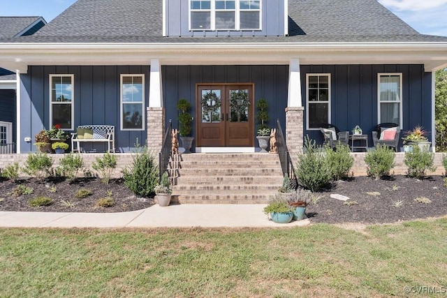 view of exterior entry with roof with shingles, a porch, board and batten siding, and brick siding