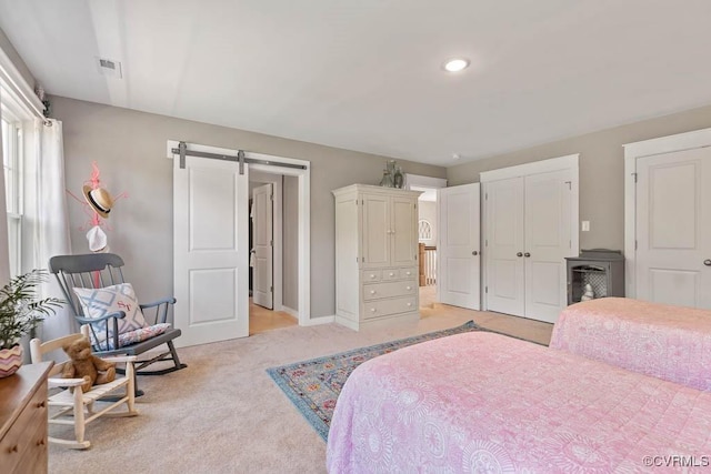 bedroom featuring light carpet, a barn door, visible vents, and baseboards