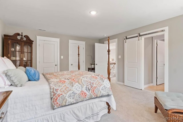 bedroom with light carpet, visible vents, baseboards, and a barn door