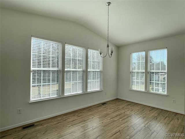 unfurnished dining area featuring baseboards, visible vents, vaulted ceiling, and wood finished floors