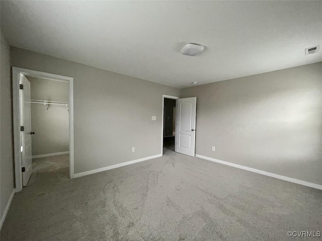 unfurnished bedroom with carpet floors, a walk in closet, a closet, visible vents, and baseboards