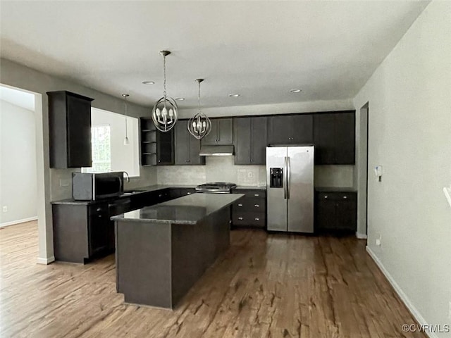 kitchen with wood finished floors, appliances with stainless steel finishes, a kitchen island, and under cabinet range hood