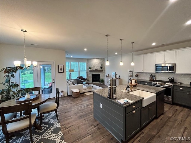 kitchen featuring a large fireplace, decorative backsplash, dark wood-style floors, appliances with stainless steel finishes, and a sink