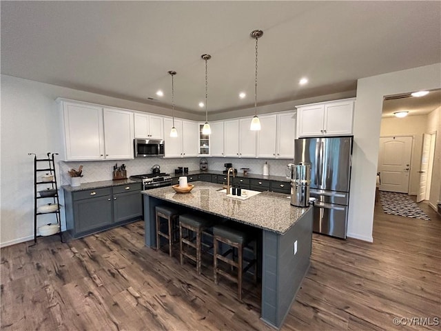 kitchen featuring a kitchen island with sink, stainless steel appliances, a sink, tasteful backsplash, and dark wood finished floors