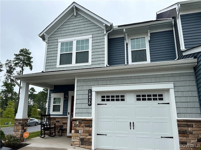 view of front of house featuring a garage, stone siding, and covered porch