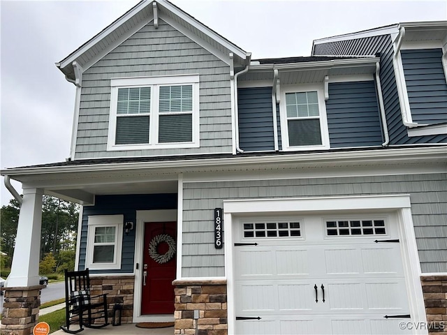 view of front of house featuring an attached garage, stone siding, and a porch