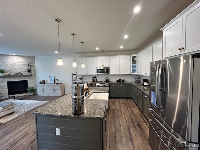 kitchen featuring dark stone counters, dark wood-style floors, appliances with stainless steel finishes, open floor plan, and a sink