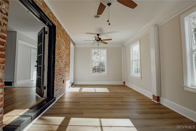 unfurnished room featuring ceiling fan, hardwood / wood-style flooring, crown molding, and brick wall