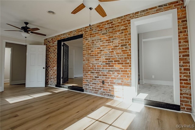 empty room featuring ceiling fan, hardwood / wood-style flooring, and brick wall