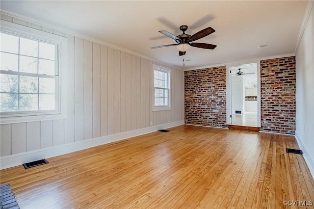 empty room with light wood-type flooring, ornamental molding, ceiling fan, and brick wall