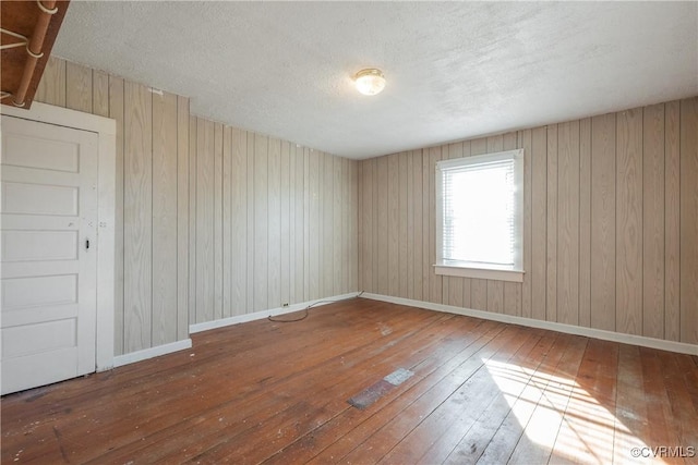 unfurnished room with hardwood / wood-style floors, wooden walls, and a textured ceiling