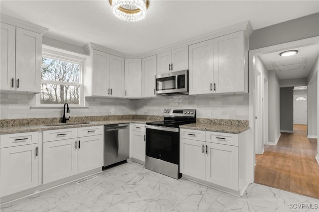 kitchen featuring stainless steel appliances, light stone counters, white cabinets, decorative backsplash, and sink