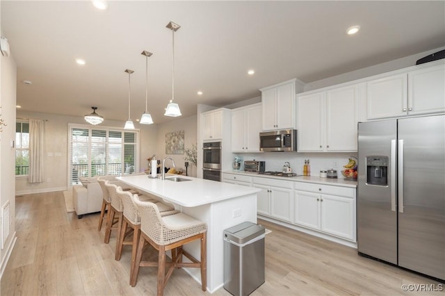 kitchen with a sink, light countertops, appliances with stainless steel finishes, an island with sink, and decorative light fixtures