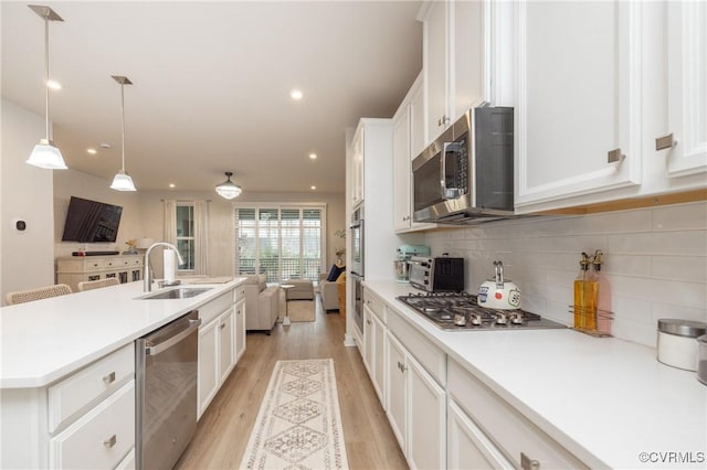 kitchen featuring stainless steel appliances, light countertops, open floor plan, white cabinets, and a sink