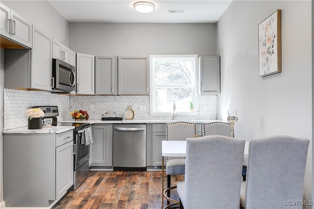 kitchen with dark hardwood / wood-style flooring, stainless steel appliances, gray cabinetry, and backsplash