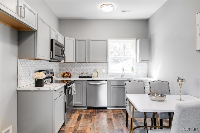 kitchen with gray cabinetry, stainless steel appliances, backsplash, dark hardwood / wood-style flooring, and sink