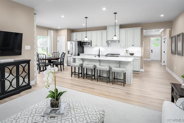 kitchen with appliances with stainless steel finishes, decorative light fixtures, white cabinets, an island with sink, and a breakfast bar area