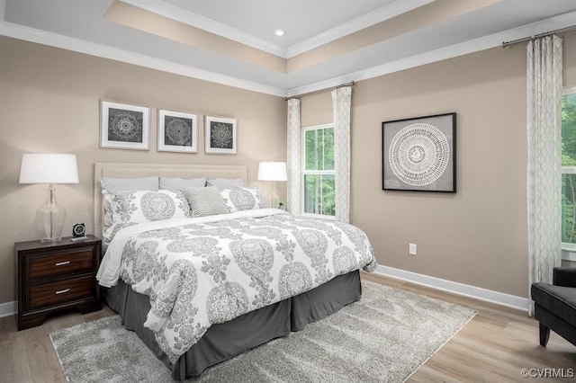 bedroom with crown molding, a tray ceiling, and light wood-type flooring