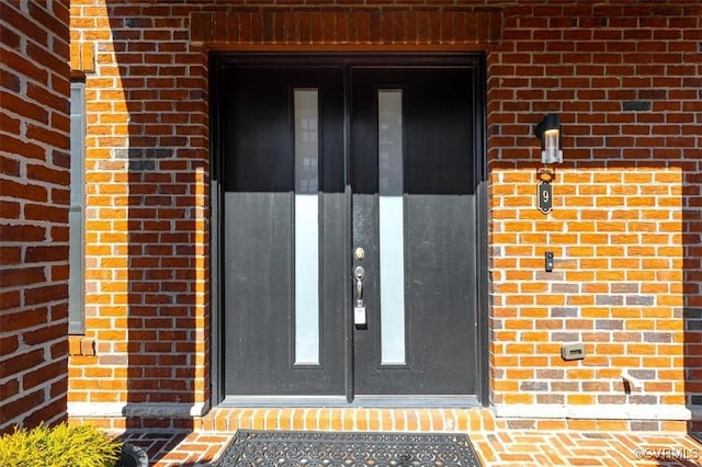 view of exterior entry with a garage and brick siding