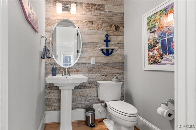 half bathroom with wood walls, wood finished floors, toilet, and baseboards