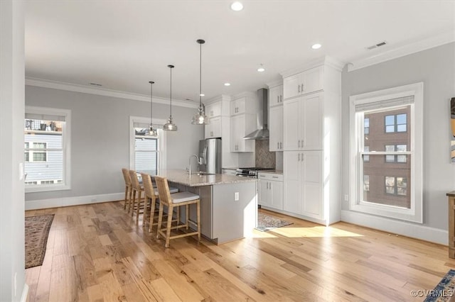 kitchen featuring appliances with stainless steel finishes, white cabinetry, a center island with sink, and wall chimney exhaust hood