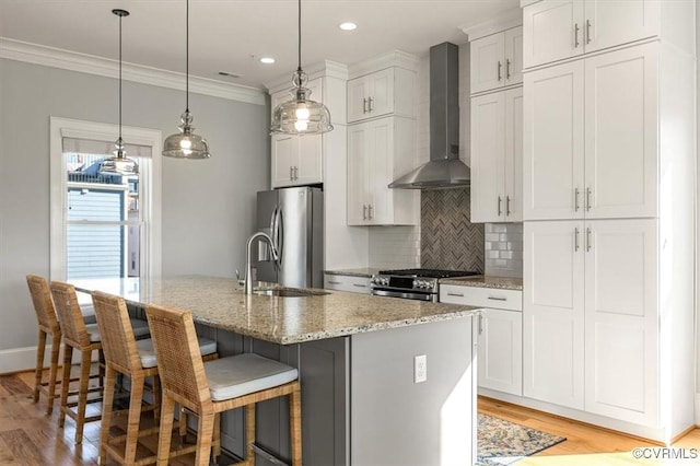 kitchen with wall chimney range hood, an island with sink, appliances with stainless steel finishes, and white cabinets