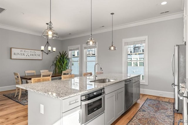 kitchen with an island with sink, stainless steel appliances, a sink, and decorative light fixtures