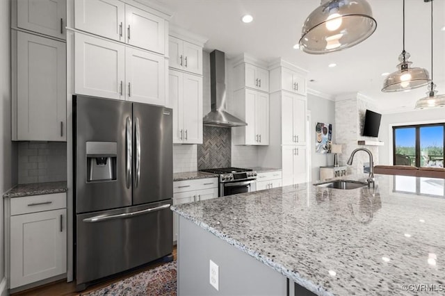 kitchen with stainless steel appliances, a sink, white cabinetry, hanging light fixtures, and wall chimney range hood