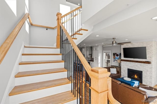 stairs with a ceiling fan, recessed lighting, and a fireplace